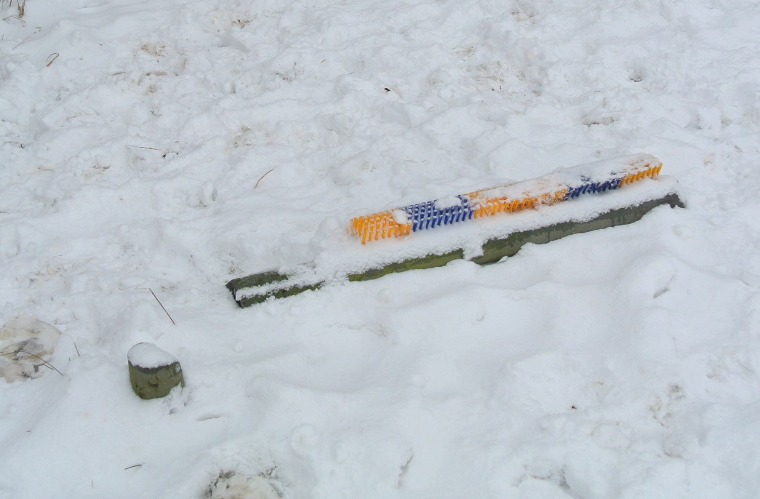 Eine bunt gefärbte Skibrille, teilweise im Schnee versteckt, liegt auf einer schneebedeckten Fläche.